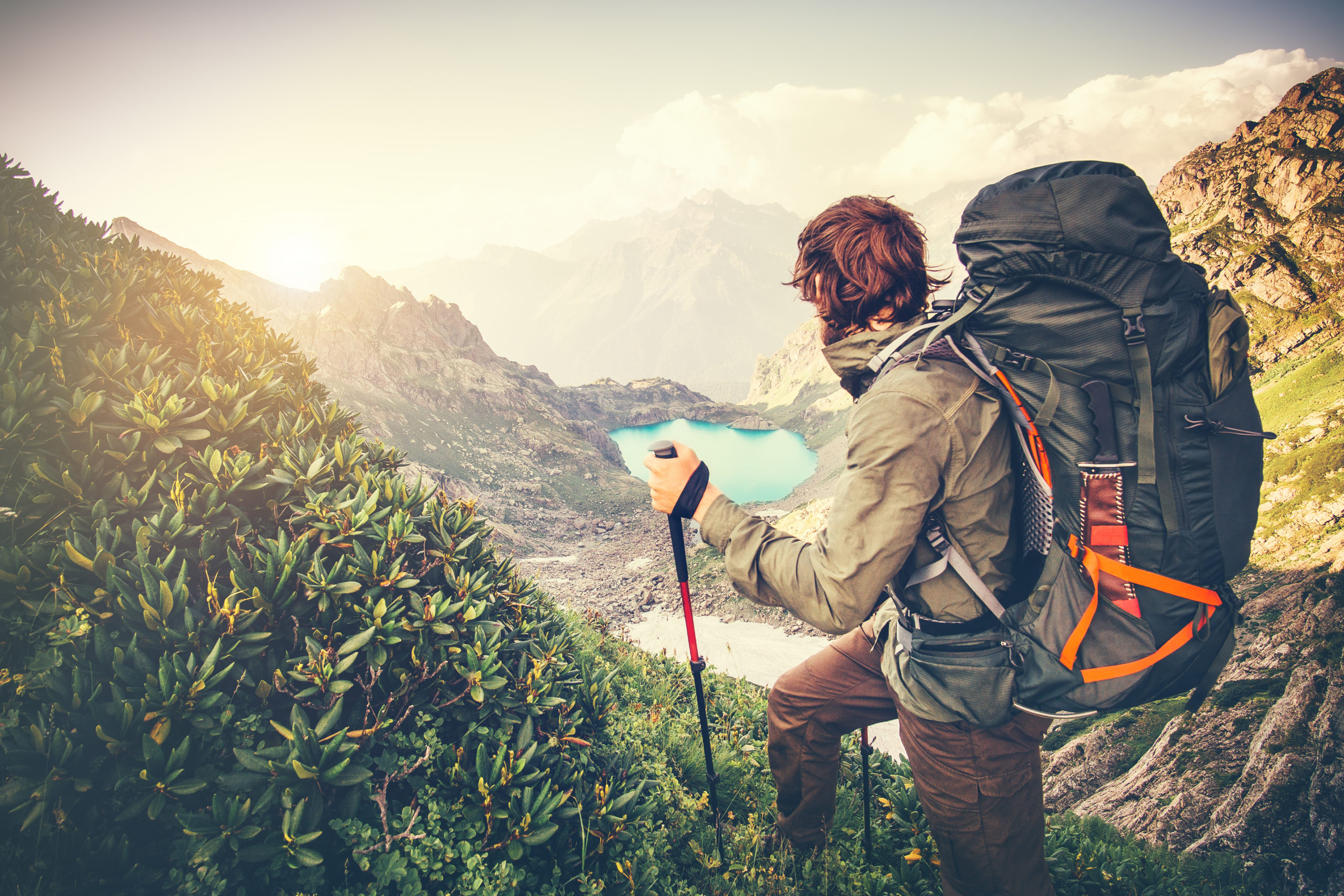 A male hiker with a backpack looks into the distance on a mountainside.